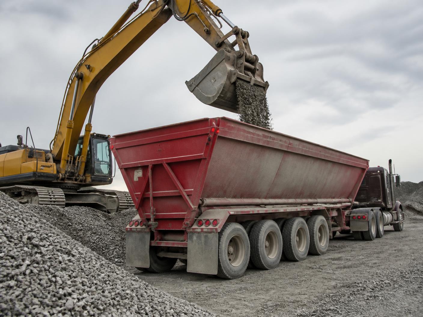Excavator loading crushed aggregate into a belly dump trailer at a materials yard